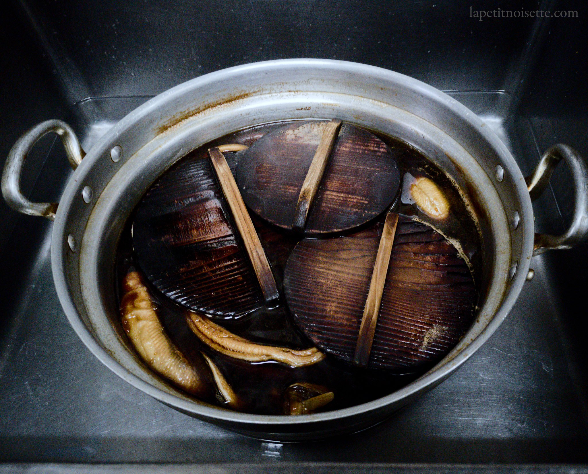 Anago being simmered in a pot with traditional wooden drop lids in a Michelin starred restaurant. 
