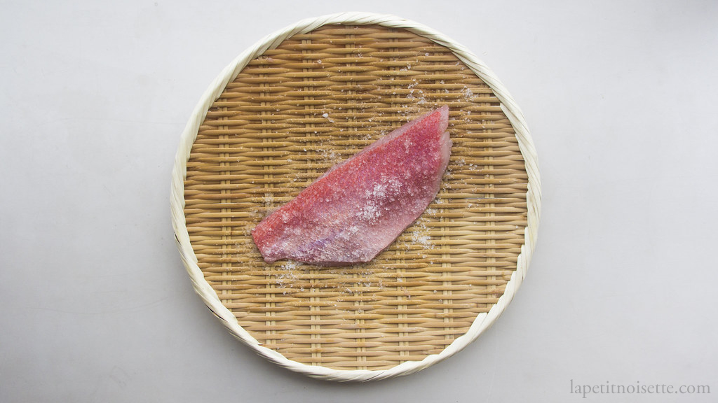 Salting a kinmedai fillet on a Japanese bamboo colander for sushi preparation.
