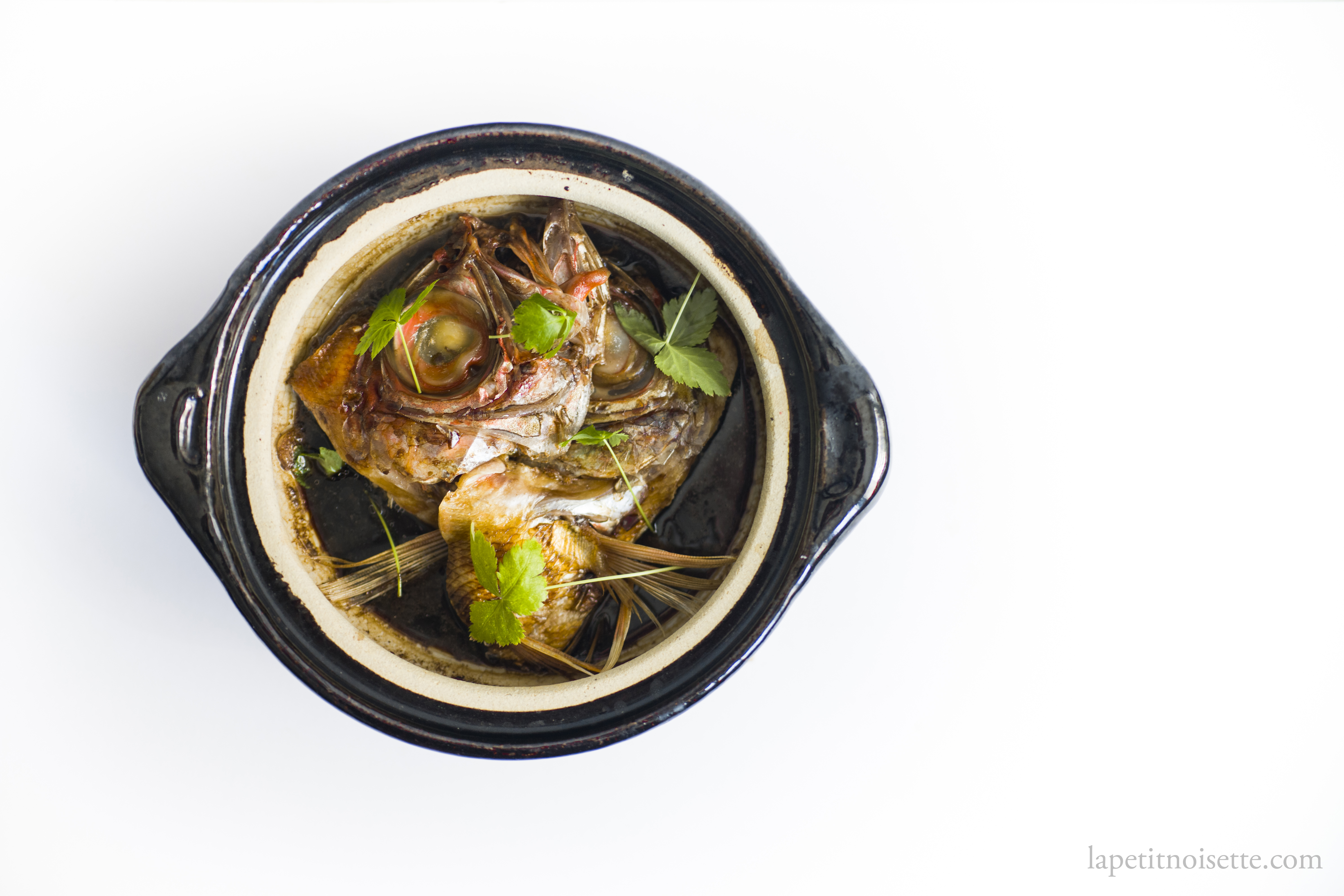 Simmered kinmedai head cooked in a donabe clay pot and garnished with mitsuba parsley.