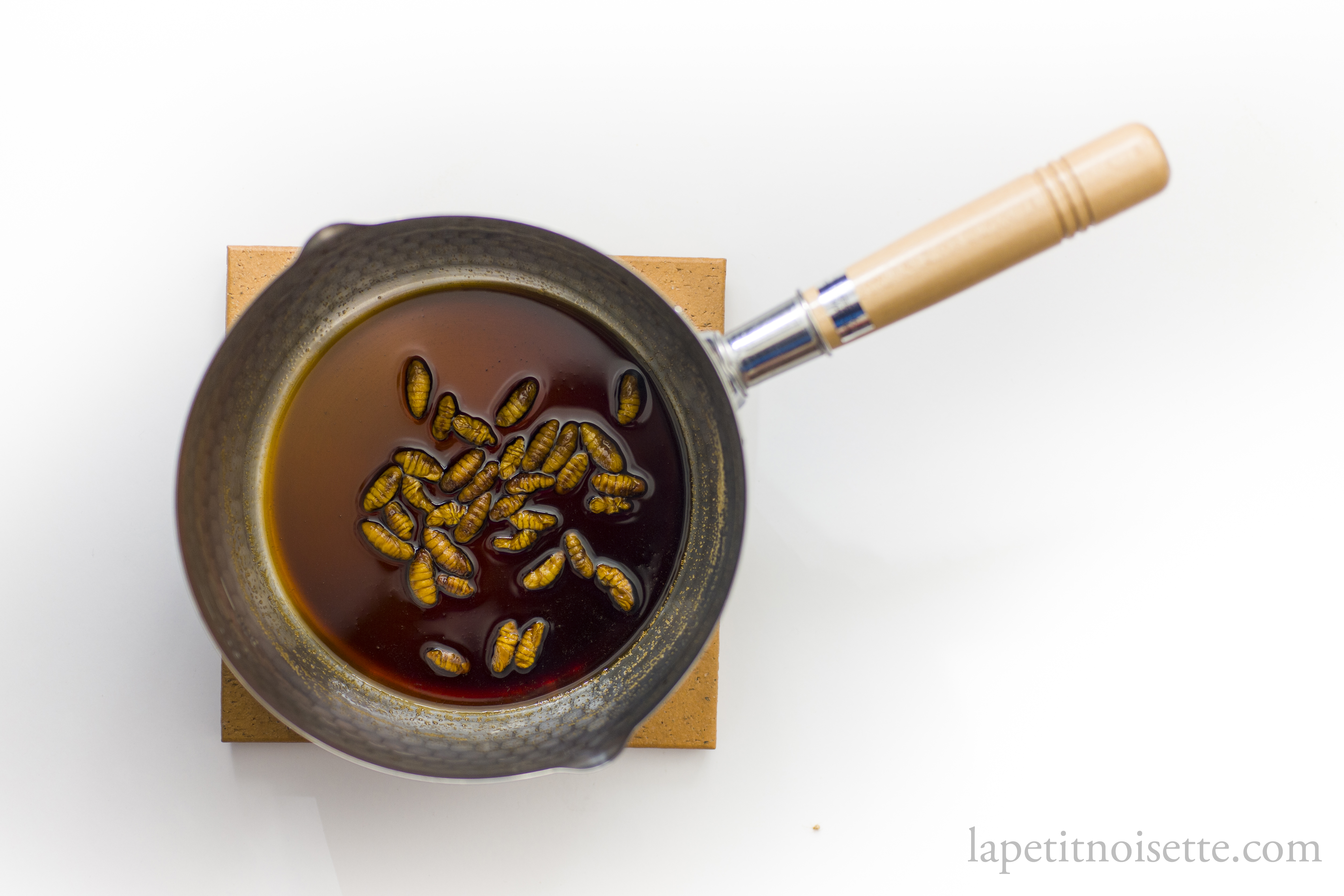Silkworm pupae being cooked in a liquid of soy sauce and sugar to glaze them into tsukudani.